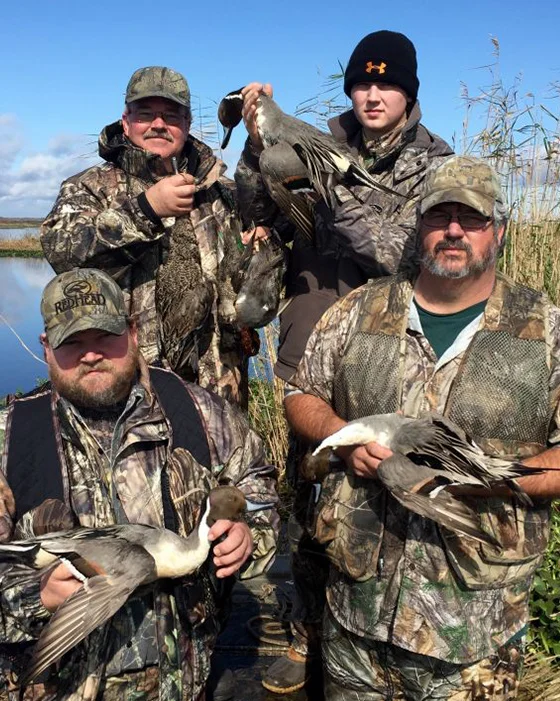 Group of hunters in camouflage holding harvested ducks in a Louisiana wetland setting, showcasing a successful duck hunting trip with Waterfowl Specialist Guide Service.